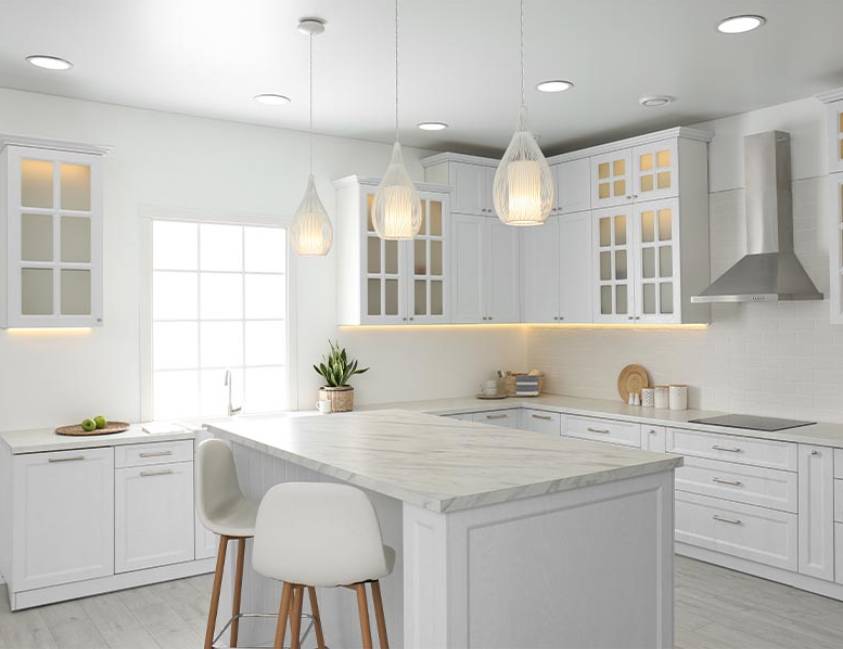 Modern kitchen interior with white cabinetry, marble countertops, and pendant lights